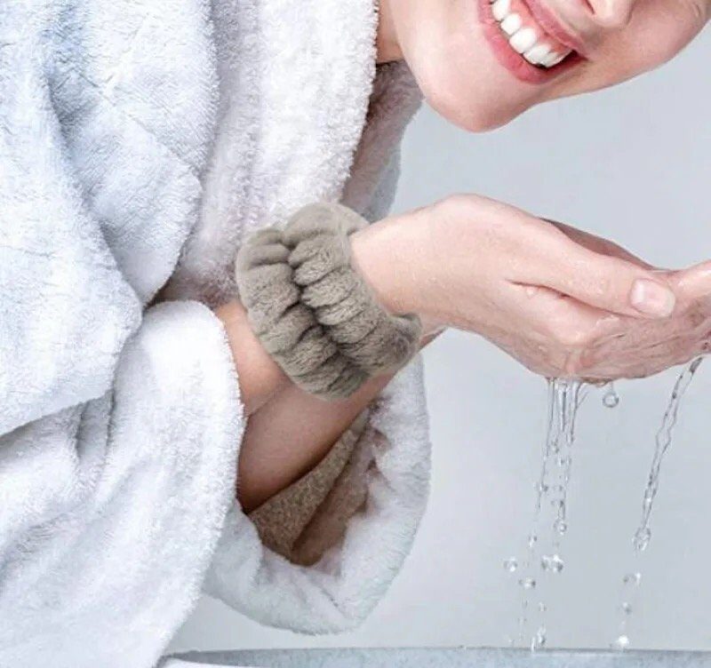 Person in bathrobe washing face, wearing fluffy wristbands to keep sleeves dry.