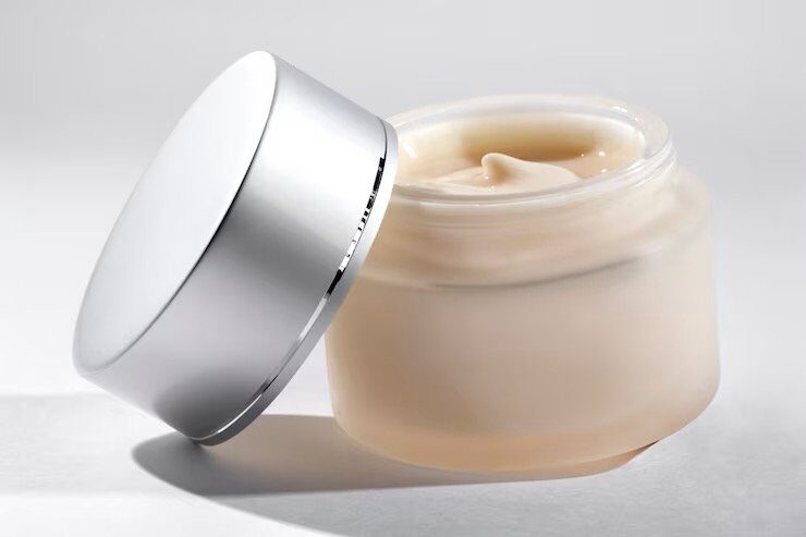 Open jar of moisturizing cream with silver lid resting beside it on a light background.