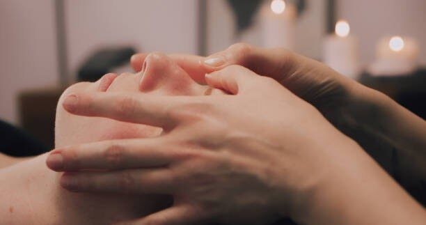 A person receives a gentle facial massage, promoting relaxation and skincare, with blurred candles in the background.