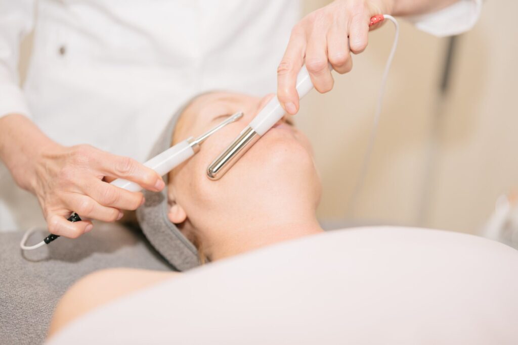 Close up of a person receiving a facial with electrical probes held by a technician in a medical setting.