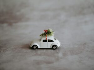 A white toy car with a Christmas tree tied to the roof with a red ribbon.