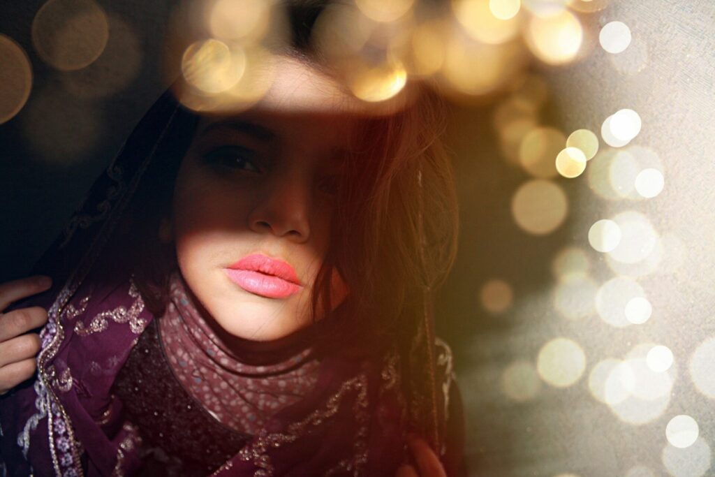 Person with pink lipstick and a headscarf, surrounded by bokeh lights, looking at the viewer.
